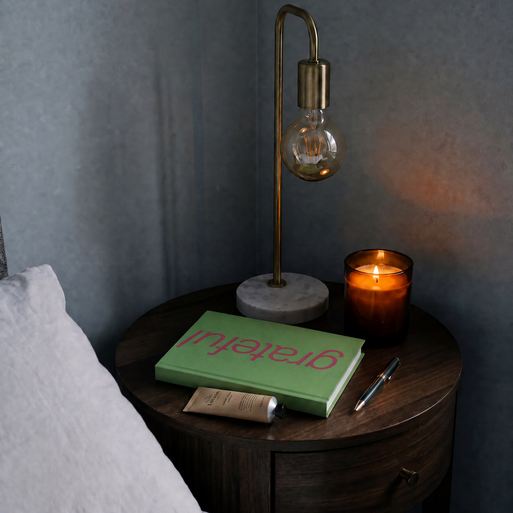 journal on bedside table with lamp and candle lit 