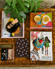 Magazines and a book on a wooden surface with a plant above them